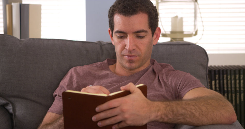 man sitting on sofa writing in a journal