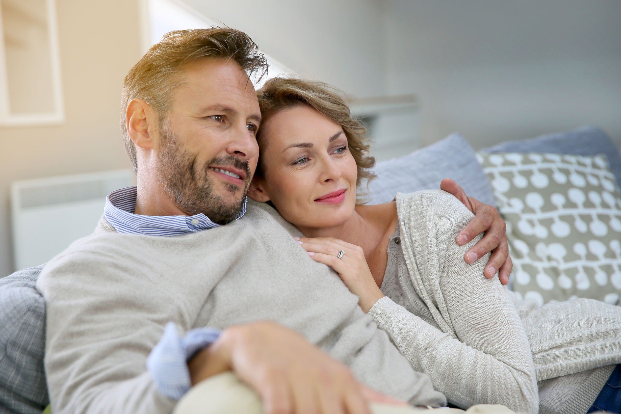middle aged couple cuddling on sofa and looking off camera
