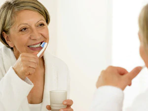 middle aged woman looking in mirror and brushing her teeth