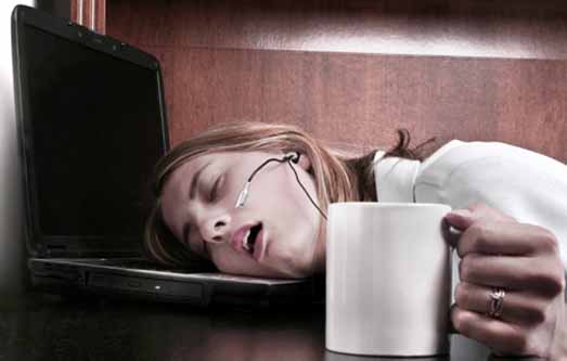 young woman at work sleeping on her laptop with cup of coffee in her hand