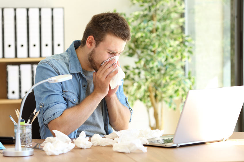 young man at work in front of a laptop with tissues in his hand and around his workspace