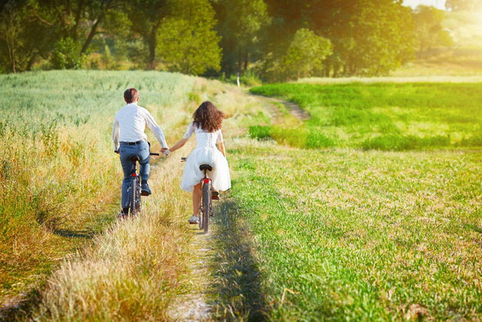 young couple holding hands and riding bikes through a field