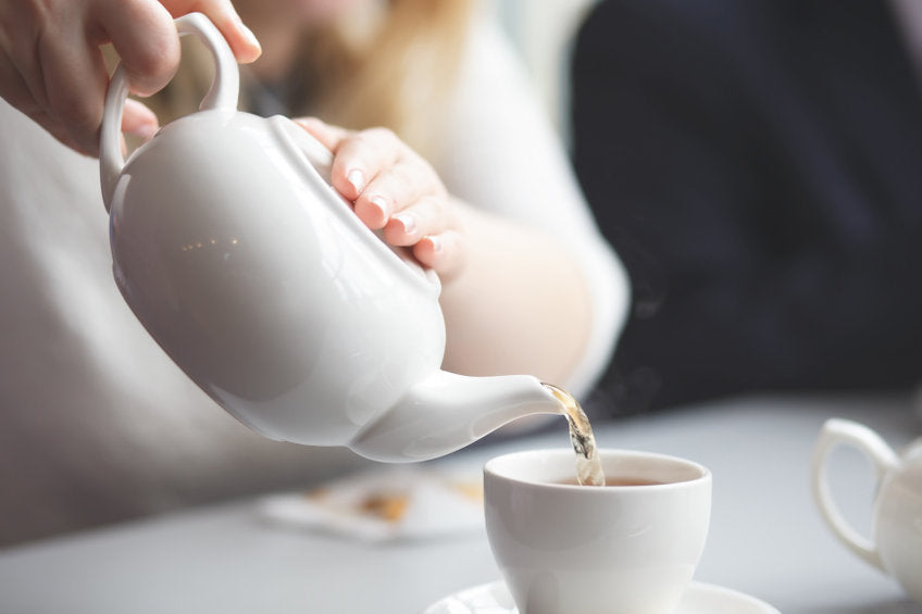 woman pouring tea from tea pot into tea cup