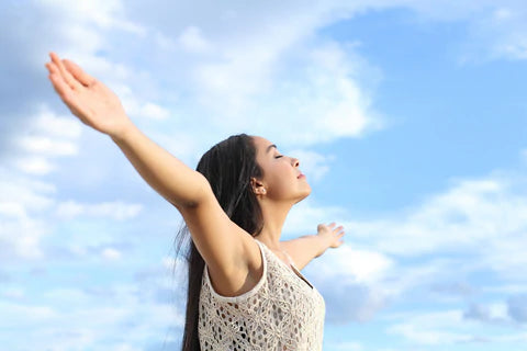 young woman with outstretched arms standing outside in sun