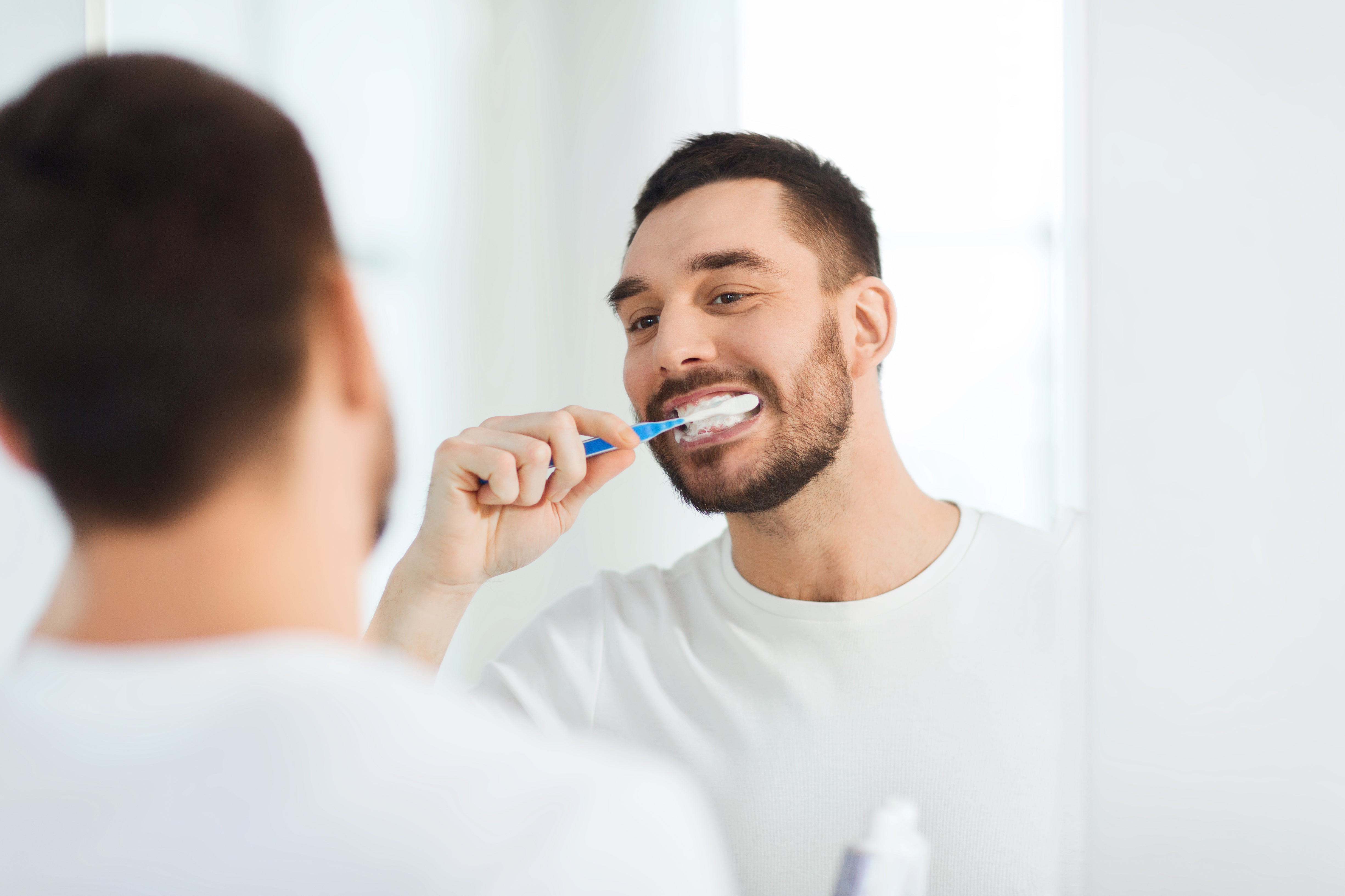 man looking in mirror brushing his teeth